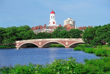 john w. weeks bridge and clock tower over charles river in harvard university campus in boston with trees and blue sky.