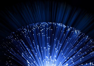 close up on the ends of many illuminated fiber optic strands with black and blue blur background.