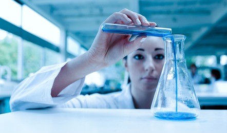 scientist pouring a liquid in an erlenmeyer flask with a test tube in a laboratory