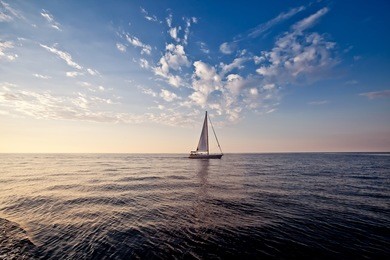 lonely yacht with white sail in open sea at sunset