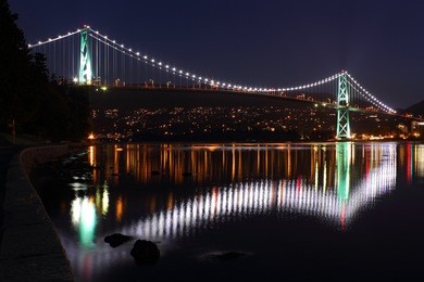 the lights of the lions gate bridge reflect in burrard inlet. seen from the seawall surrounding stanley park. vancouver, british columbia.