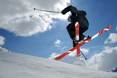 a free-ride ski jumper, with skis crossed against a blue sky with clouds