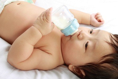 little baby boy drinks milk from bottle holded by him self, lying on bed
