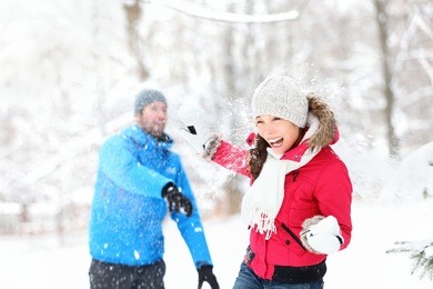 snowball fight. winter couple having fun playing in snow outdoors. young joyful happy multi-racial couple.