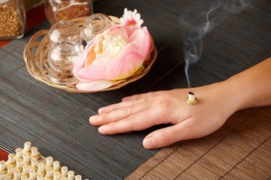 tcm traditional chinese medicine. smoking mini moxa stick, flower and natural herbs in glass jars in background.