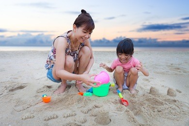 mother with children playing with sand on beach
