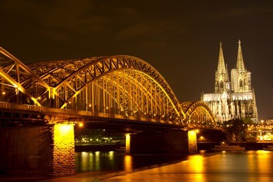riverside view of the cologne cathedral and railway bridge over the rhine river in germany at night