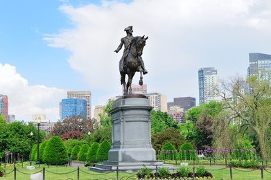 george washington statue as the famous landmark in boston common park with city skyline and skyscrapers.