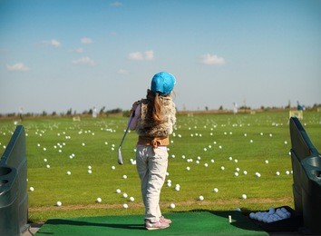 little girl swinging golf club, rear view