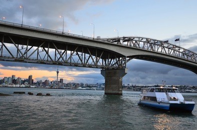 auckland harbor bridge and ferry with auckland city cbd at sunset in auckland, new zealand.