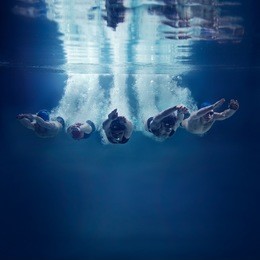 five swimmers jumping together into water isolated blue background