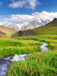 river on green meadow. high mountains and bright sky with clouds