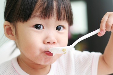 toddler girl feeding herself with a spoon of porridge