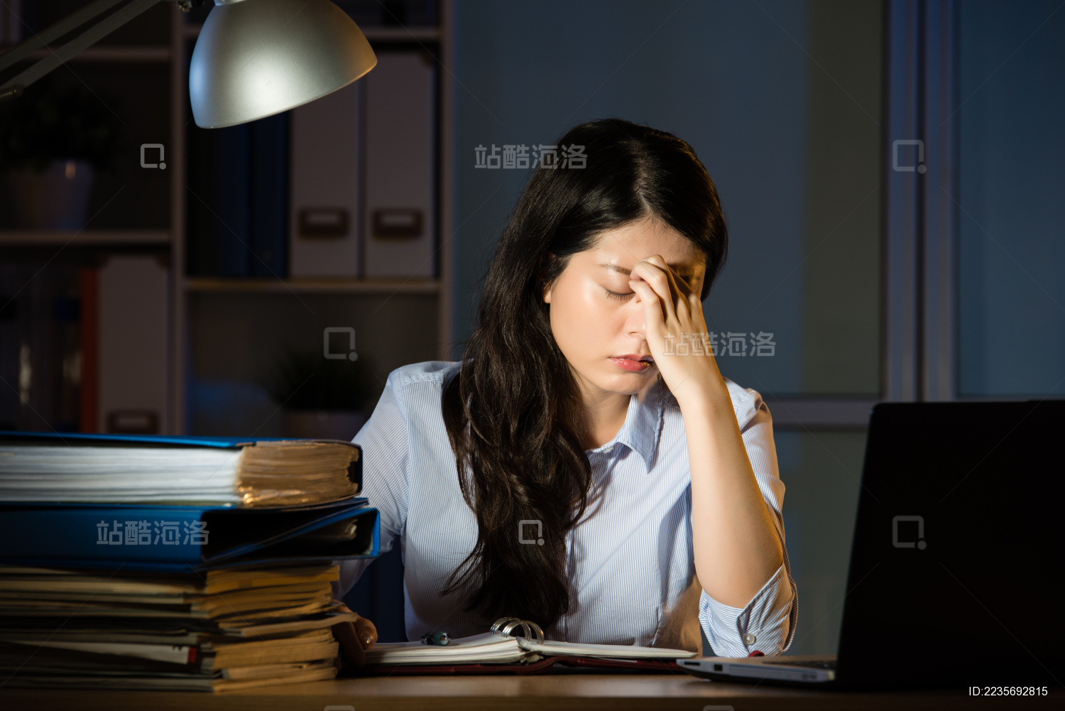 亚裔女商人坐在办公桌头痛加班深夜。在室内办公背景