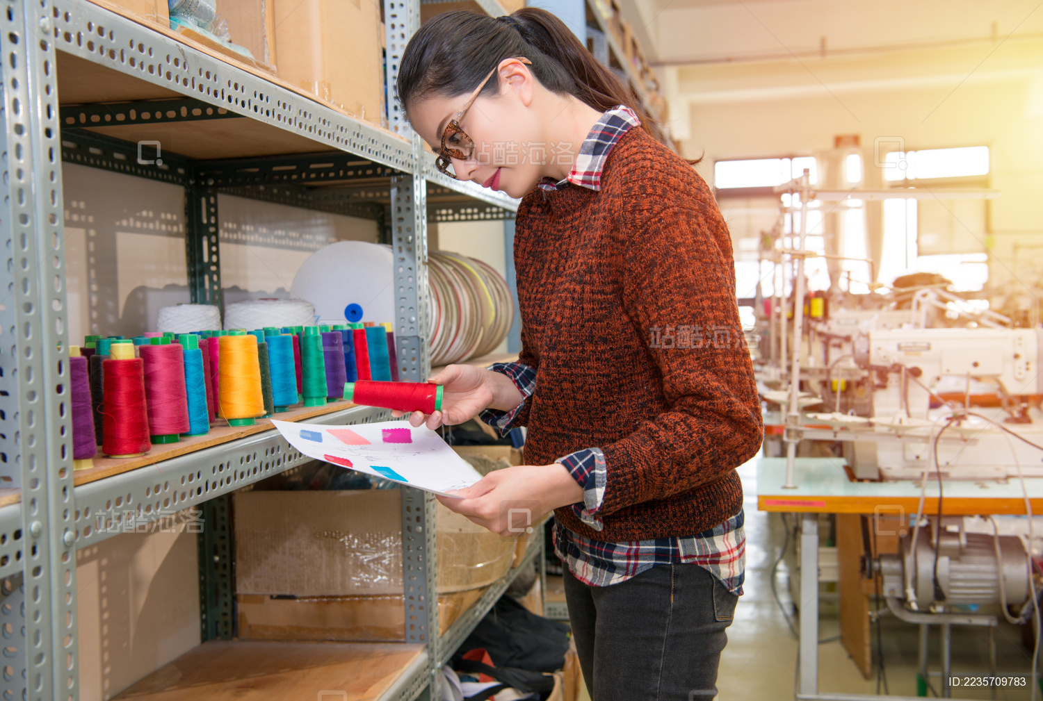 认真成功的设计师女子站在五颜六色的卷轴线程柜前 与时尚服装缝纫工作室纸样检查选择红色。