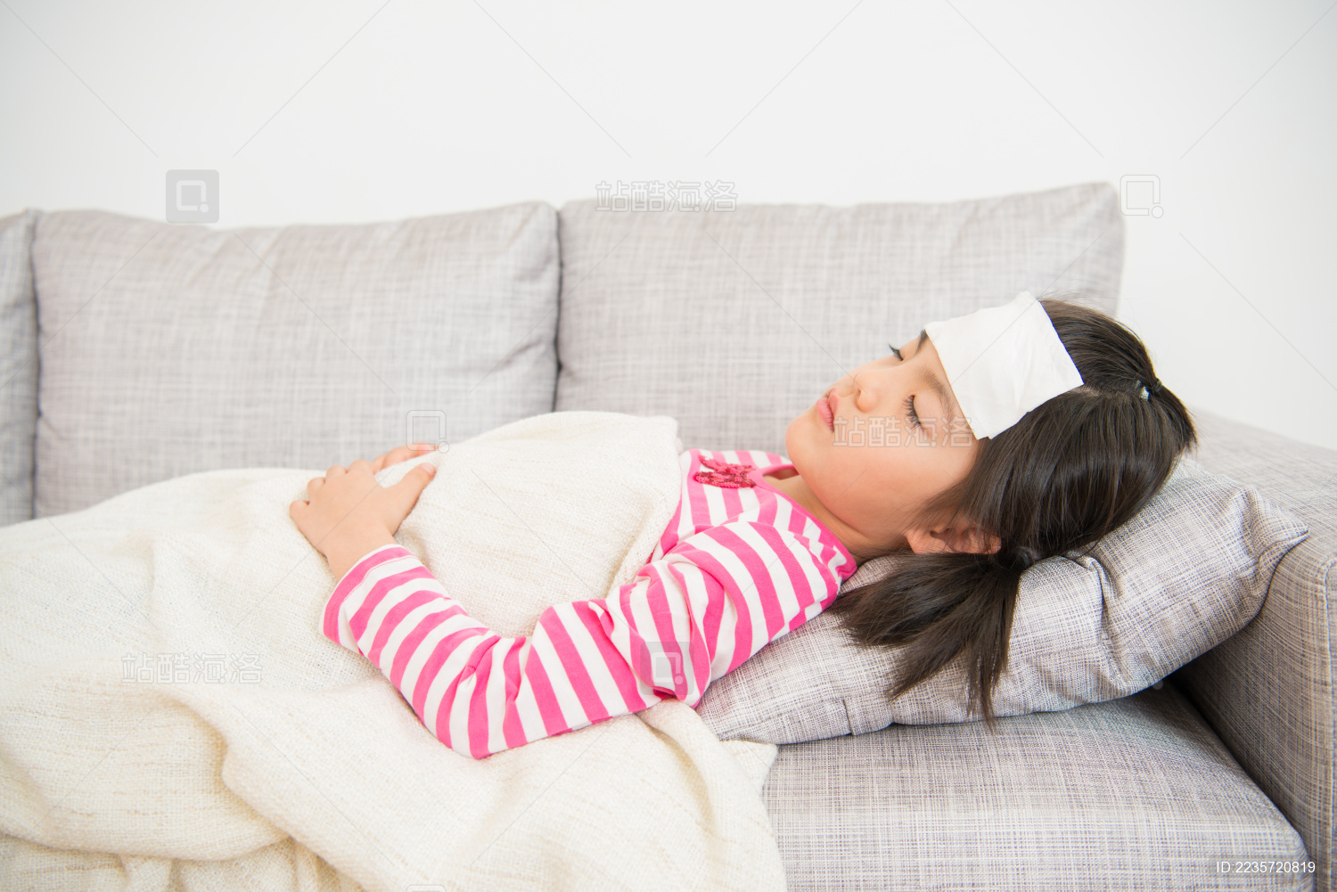 年轻女孩睡觉和生病与她的头冷凝胶。和他的妈妈照顾尝试搁在客厅在家沙发。家庭活动的概念。