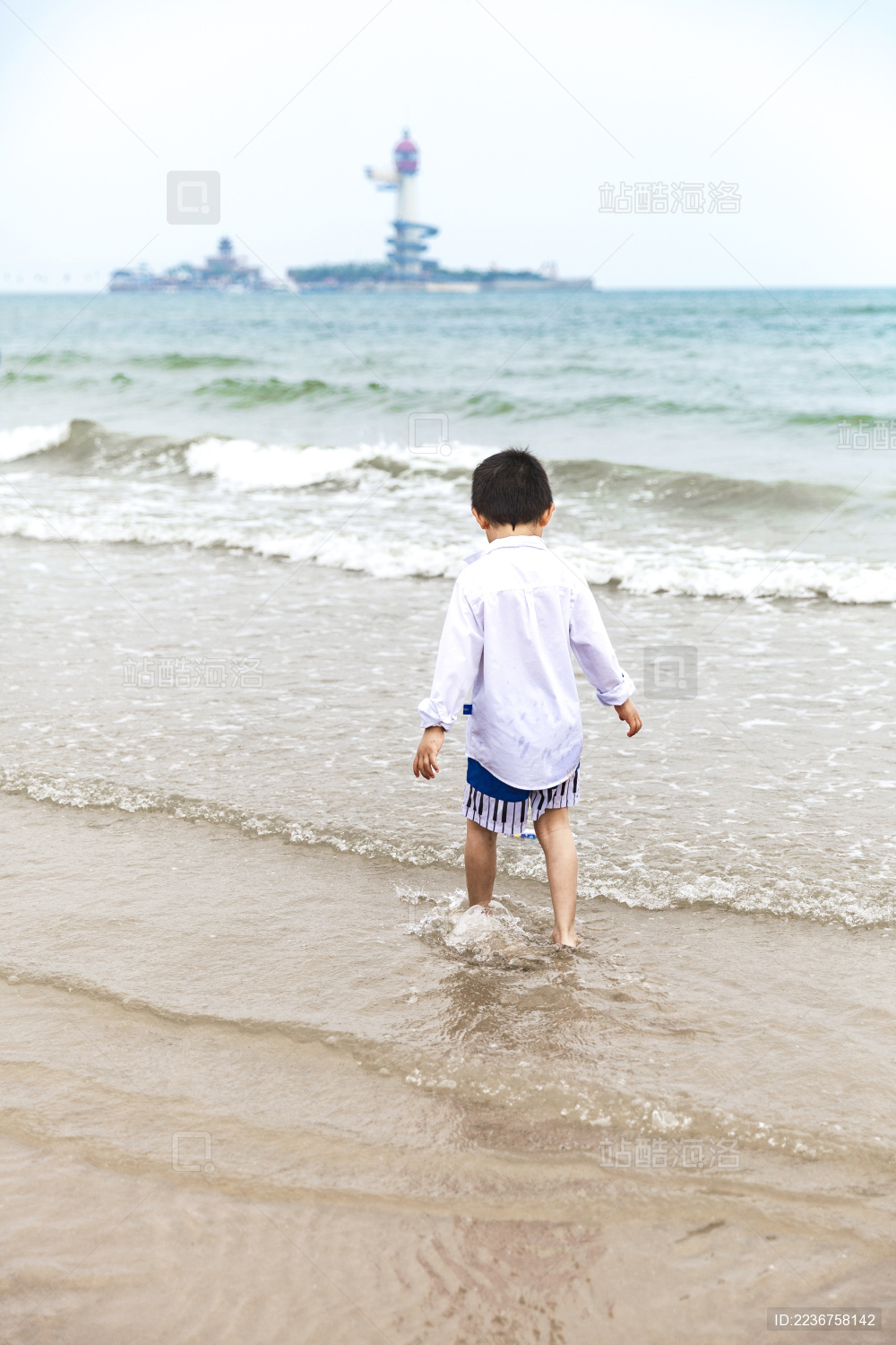 蓝天白云海边浅滩玩水的男童背影