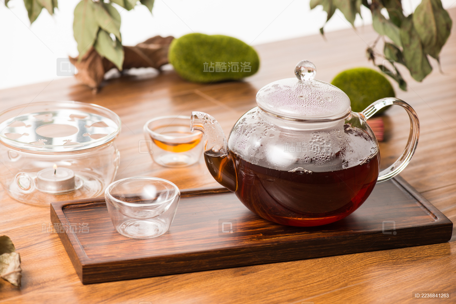 透明玻璃茶壶和两个透明玻璃小茶杯在红木仿古茶盘上冲泡红茶的场景 背景是原木色桌面和绿色植物
