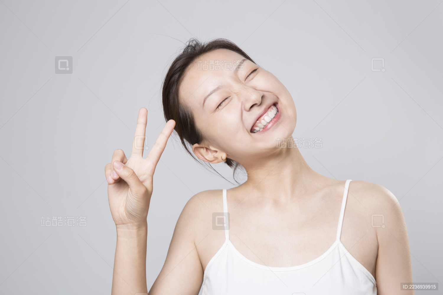 站在纯色背景前比出胜利手势的亚洲女孩开心大笑