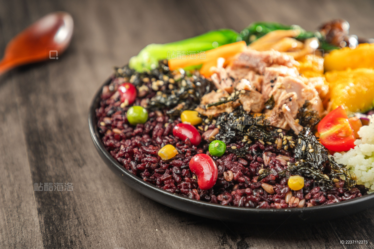 暗色木纹桌面上放着一盘金枪鱼南瓜黑米饭简餐