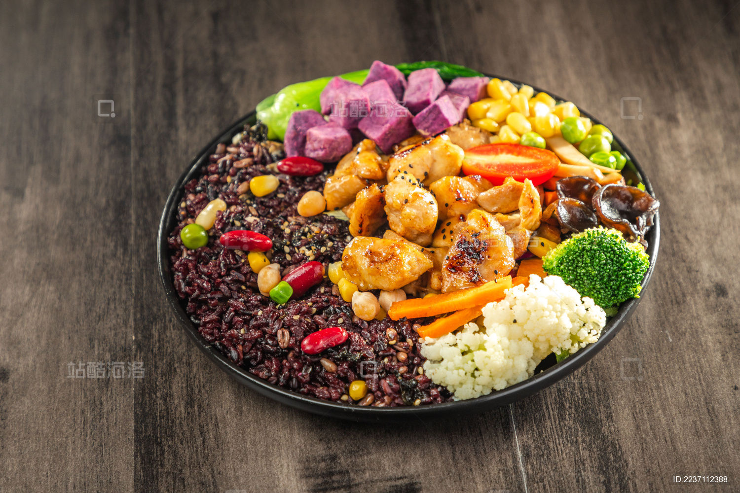  暗色木纹桌上放着一盘煎鸡腿肉黑米饭简餐