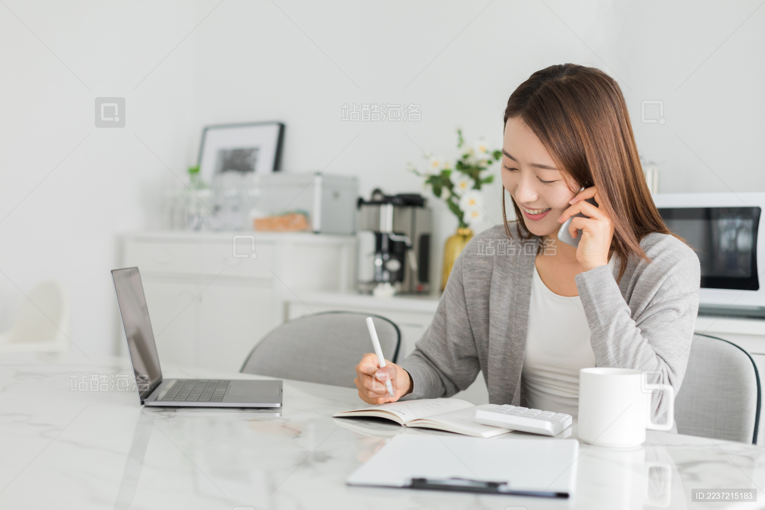 年轻女性在家坐在餐坐前一边工作一边使用手机