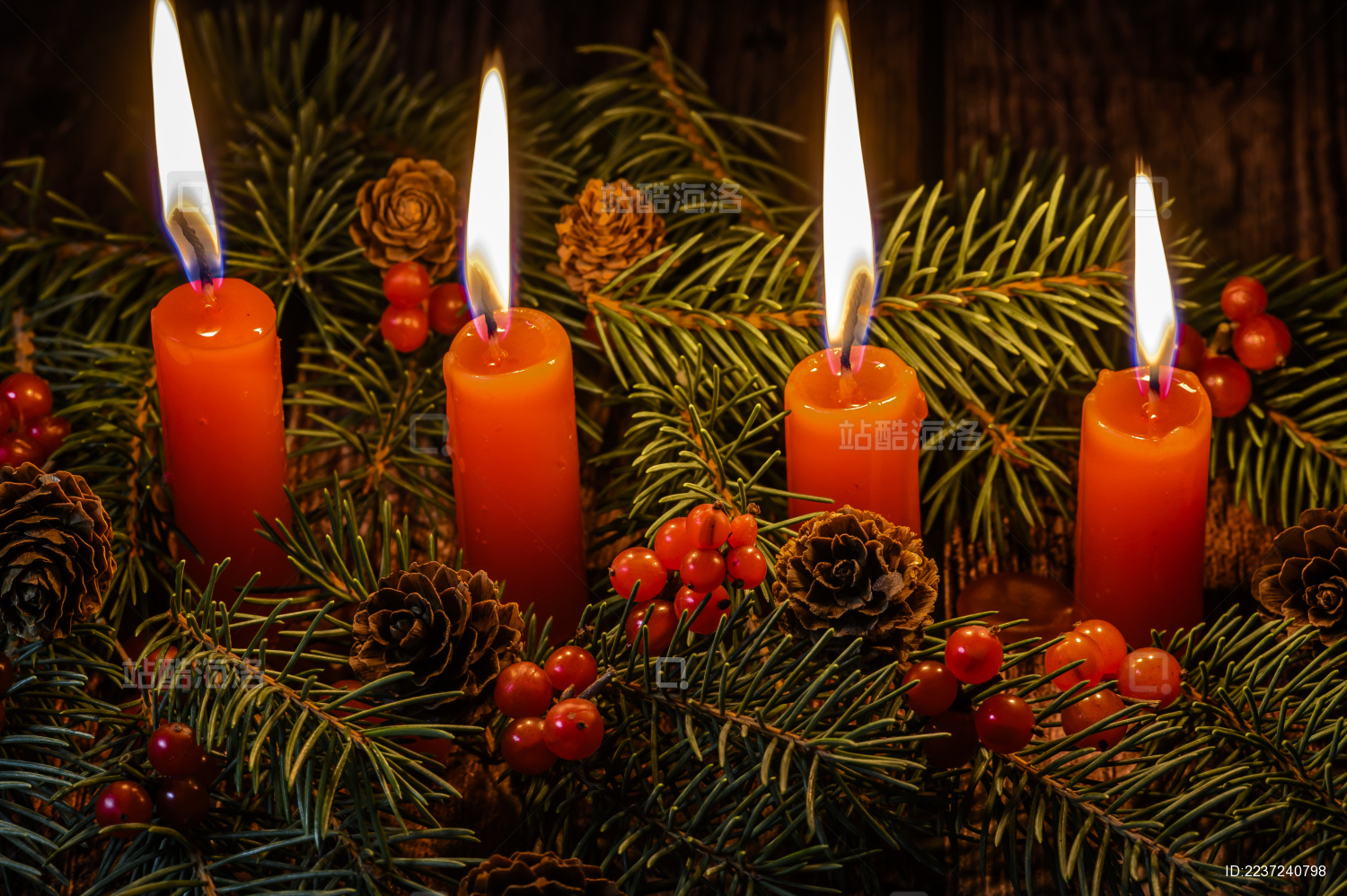 摆放在木质桌面上的圣诞树、红浆果和燃烧中的红色蜡烛