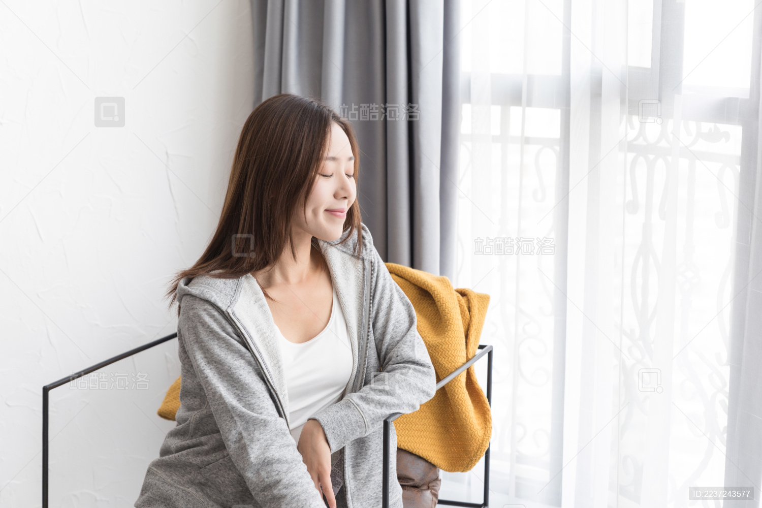 一名年轻女性坐在窗边的沙发椅上休息