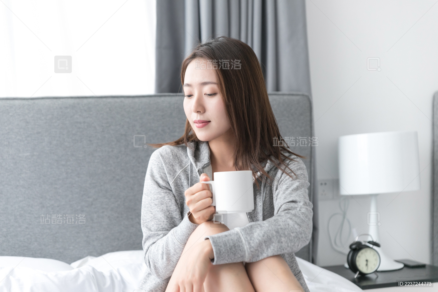 一名年轻女性坐在卧室床上喝水