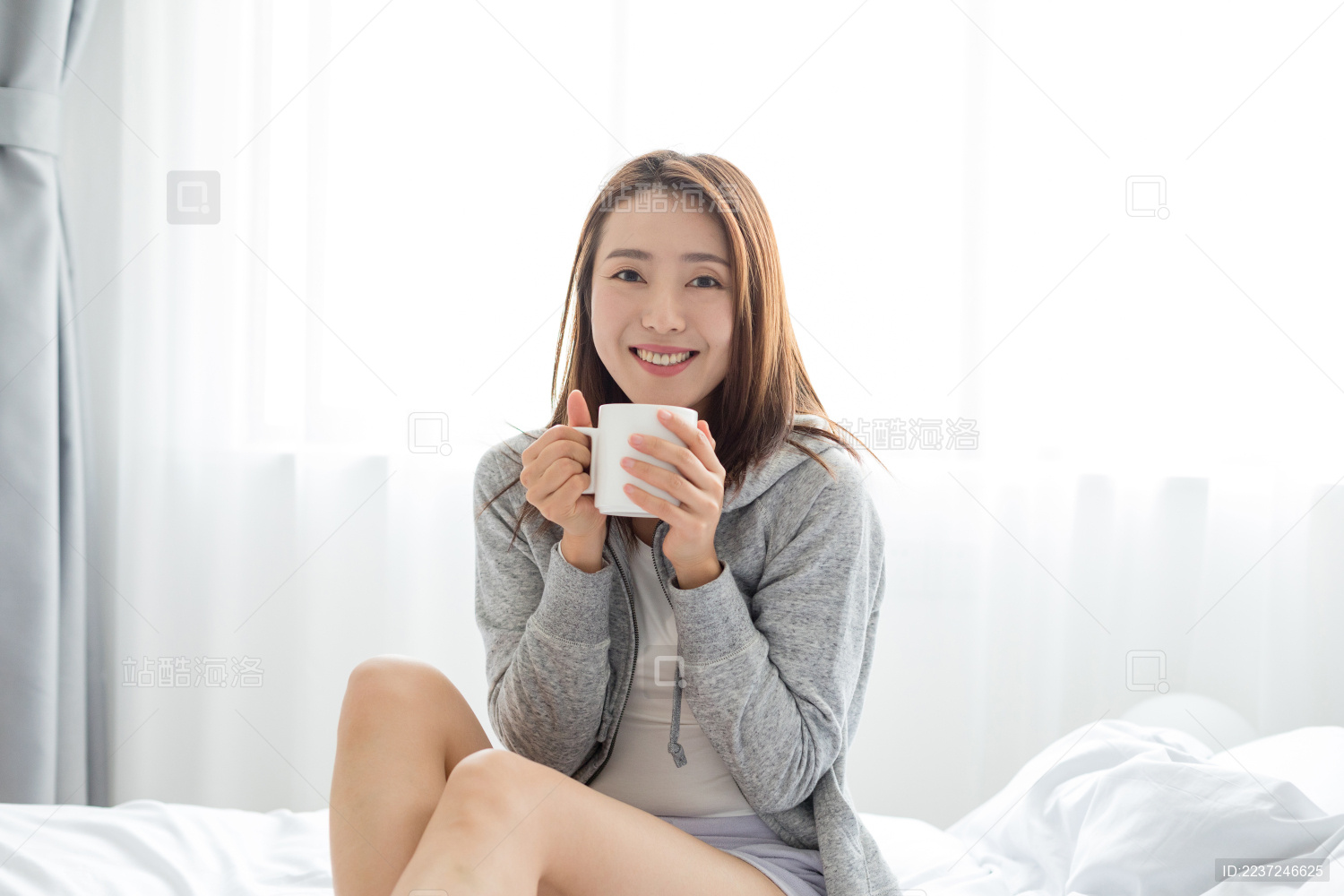 一名年轻女性坐在床上拿着水杯喝水