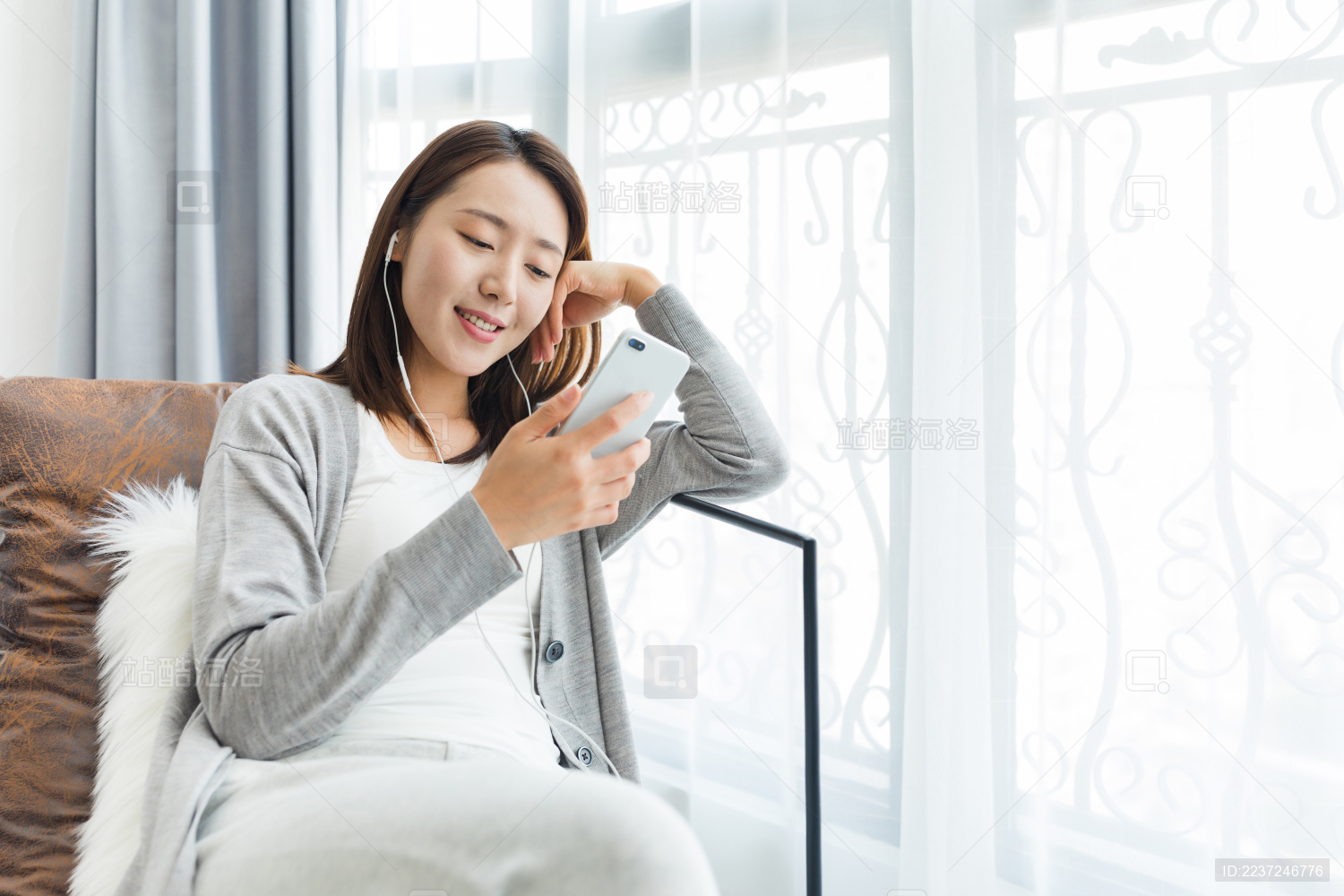 年轻女性在家烤着沙发使用手机听音乐