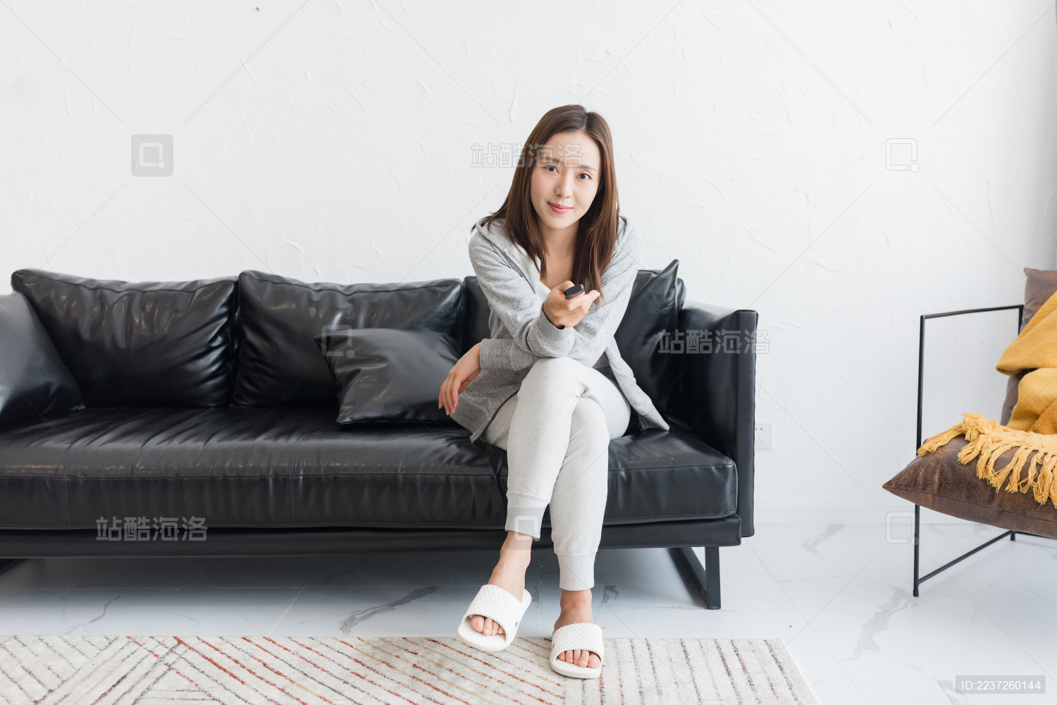 一个年轻女性坐在沙发上手拿遥控器看电视