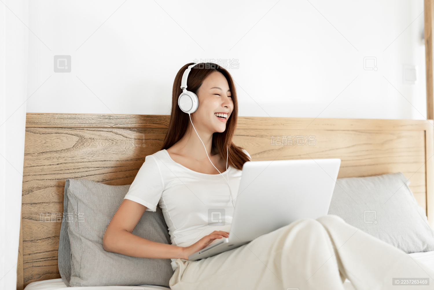 一位年轻女性在床上一边使用笔记本电脑一边听