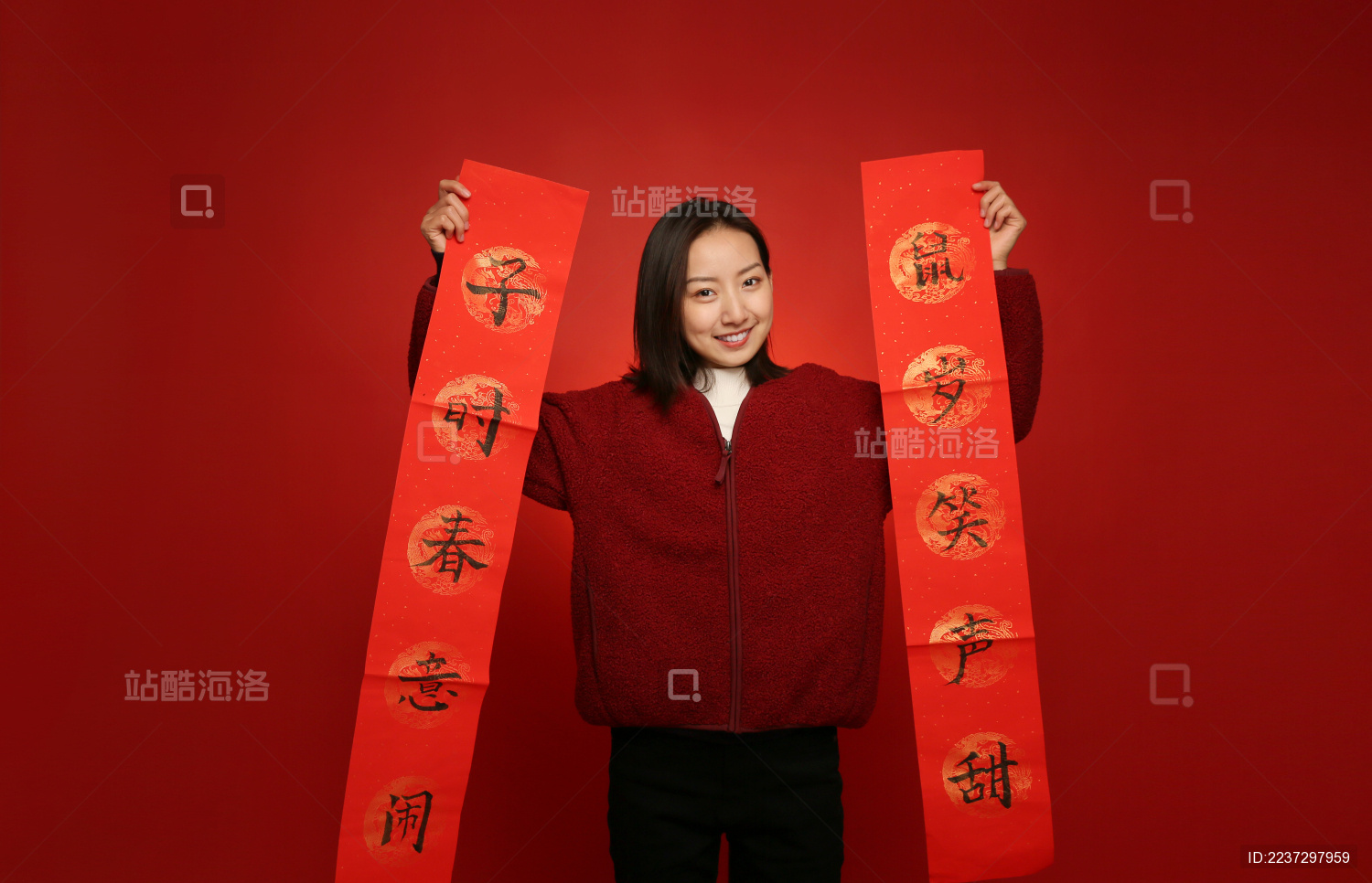 站在红色背景墙前的年轻女人手里拿着新年对联开心微笑