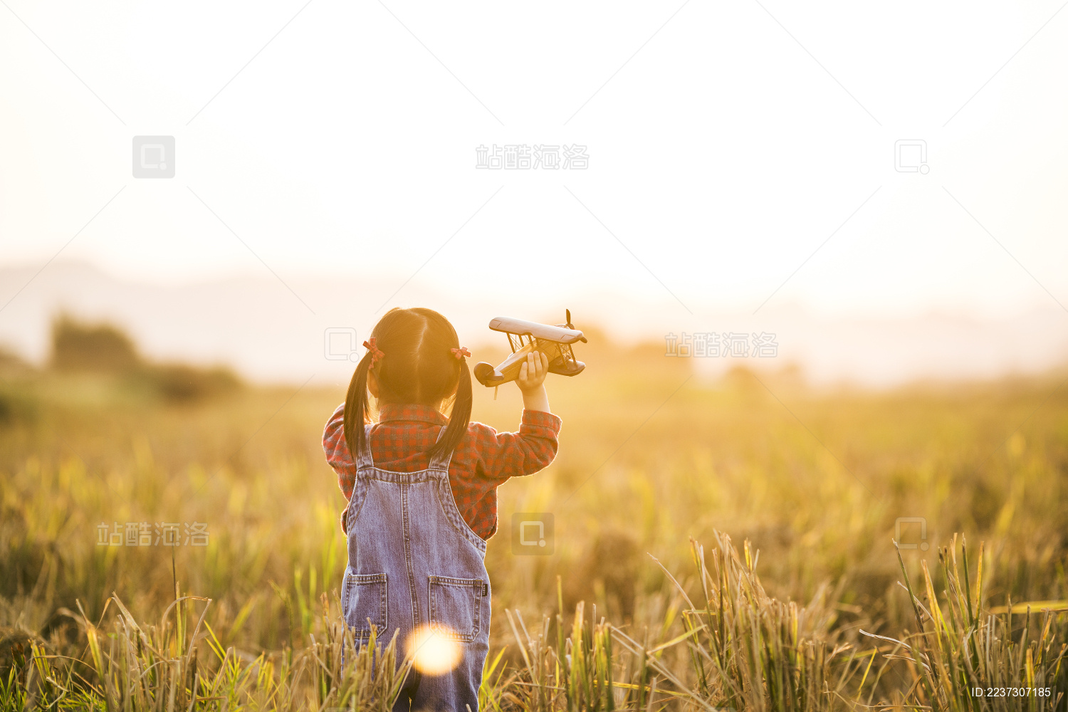 女孩子拿着模型飞机在田野玩耍