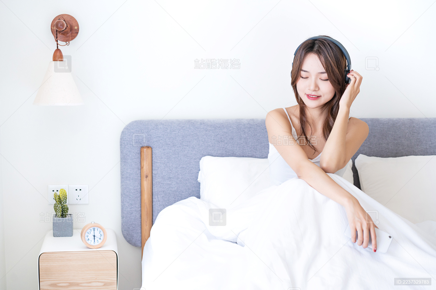 一名年轻的亚洲女子坐在床上用无线头戴耳机听