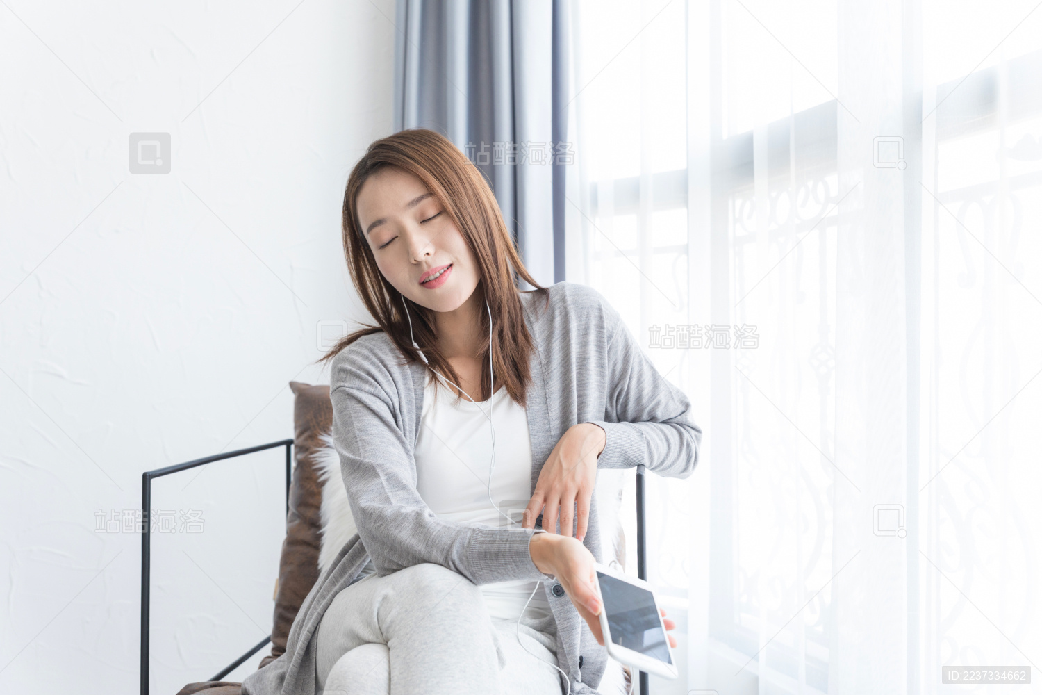 一名年轻女性坐在沙发椅上使用手机听歌