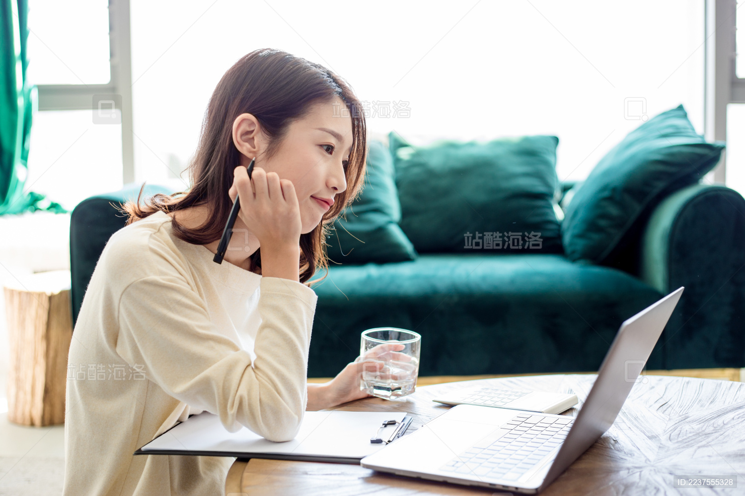 一名年轻女姓在客厅里一边办公一边喝水