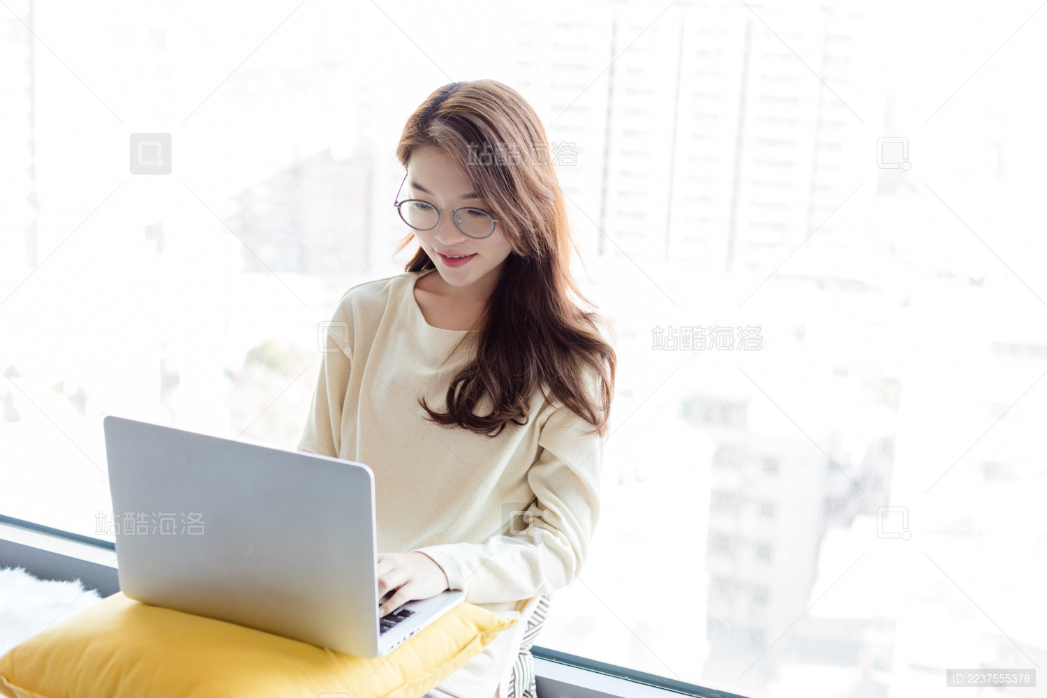 一名戴眼镜的年轻女性在窗台上使用手提电脑