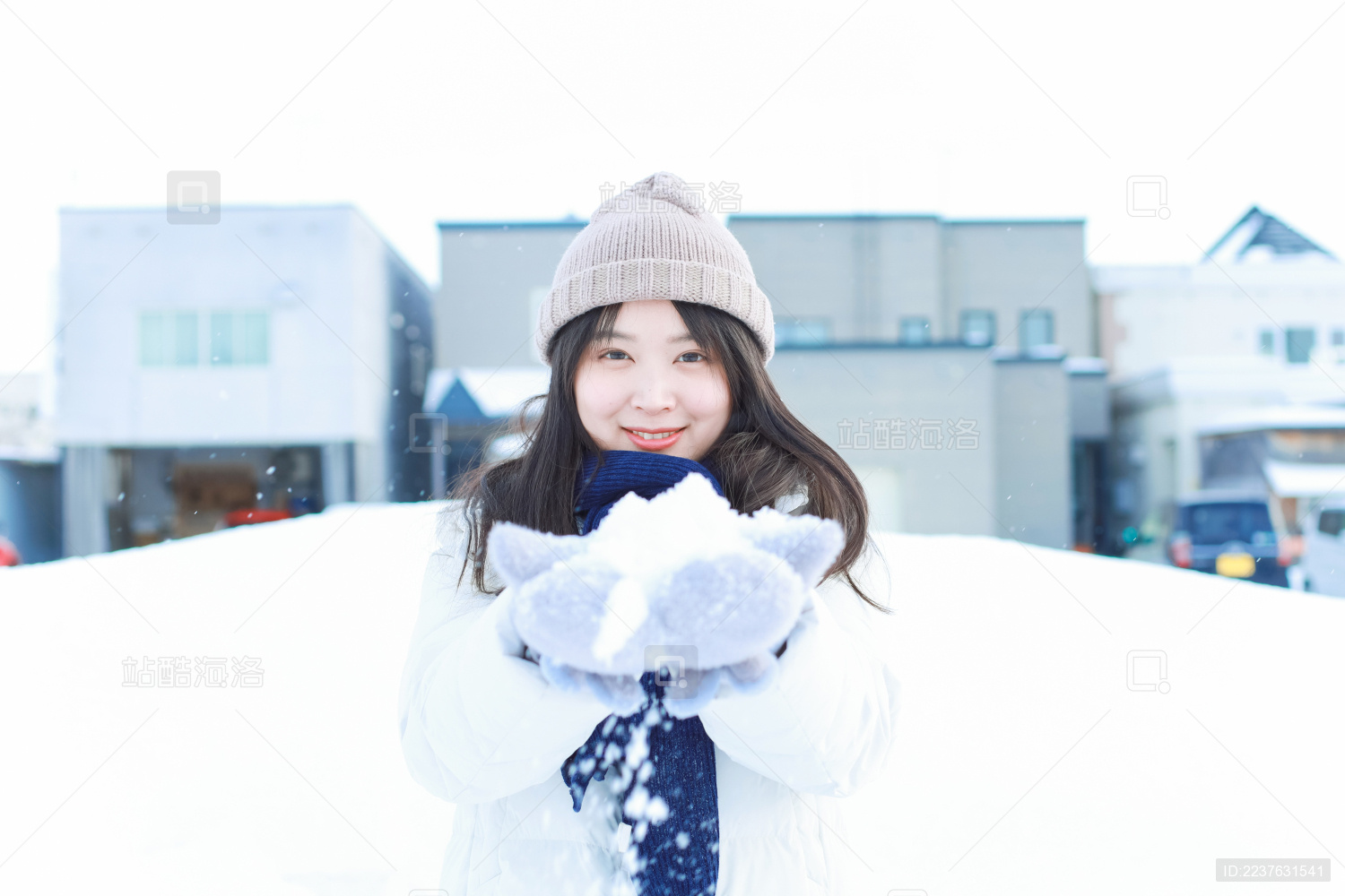 戴帽子的长发亚洲女子在雪地里微笑的捧着雪