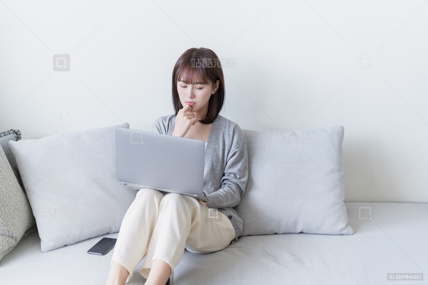 亚洲女生坐在沙发上一边看电脑一边思考