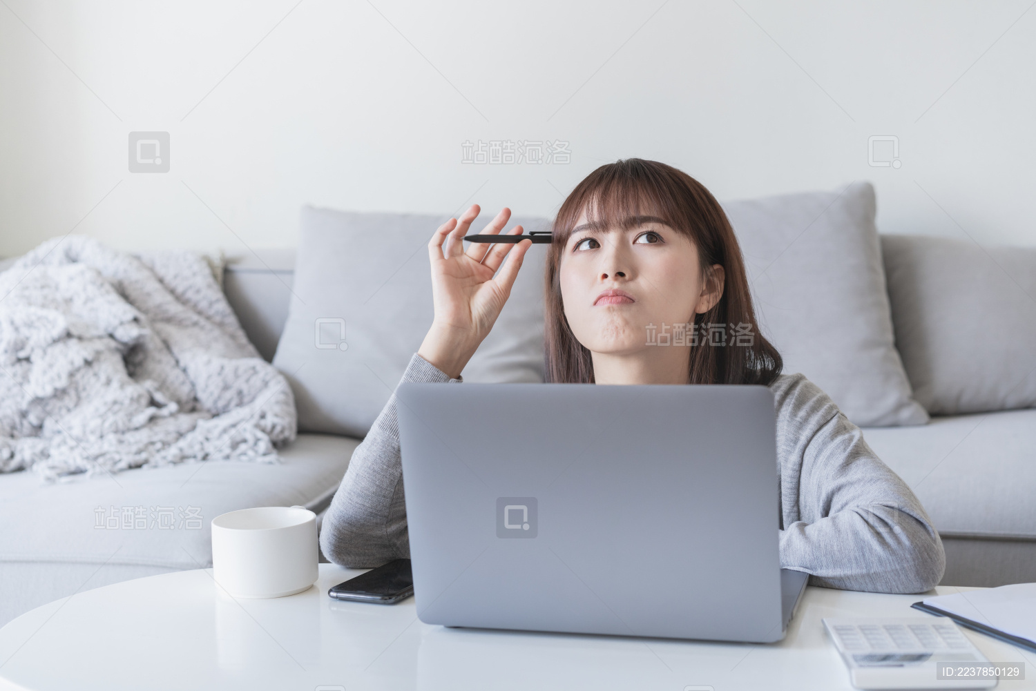 女生在手提电脑前用笔抵着脑袋在思考