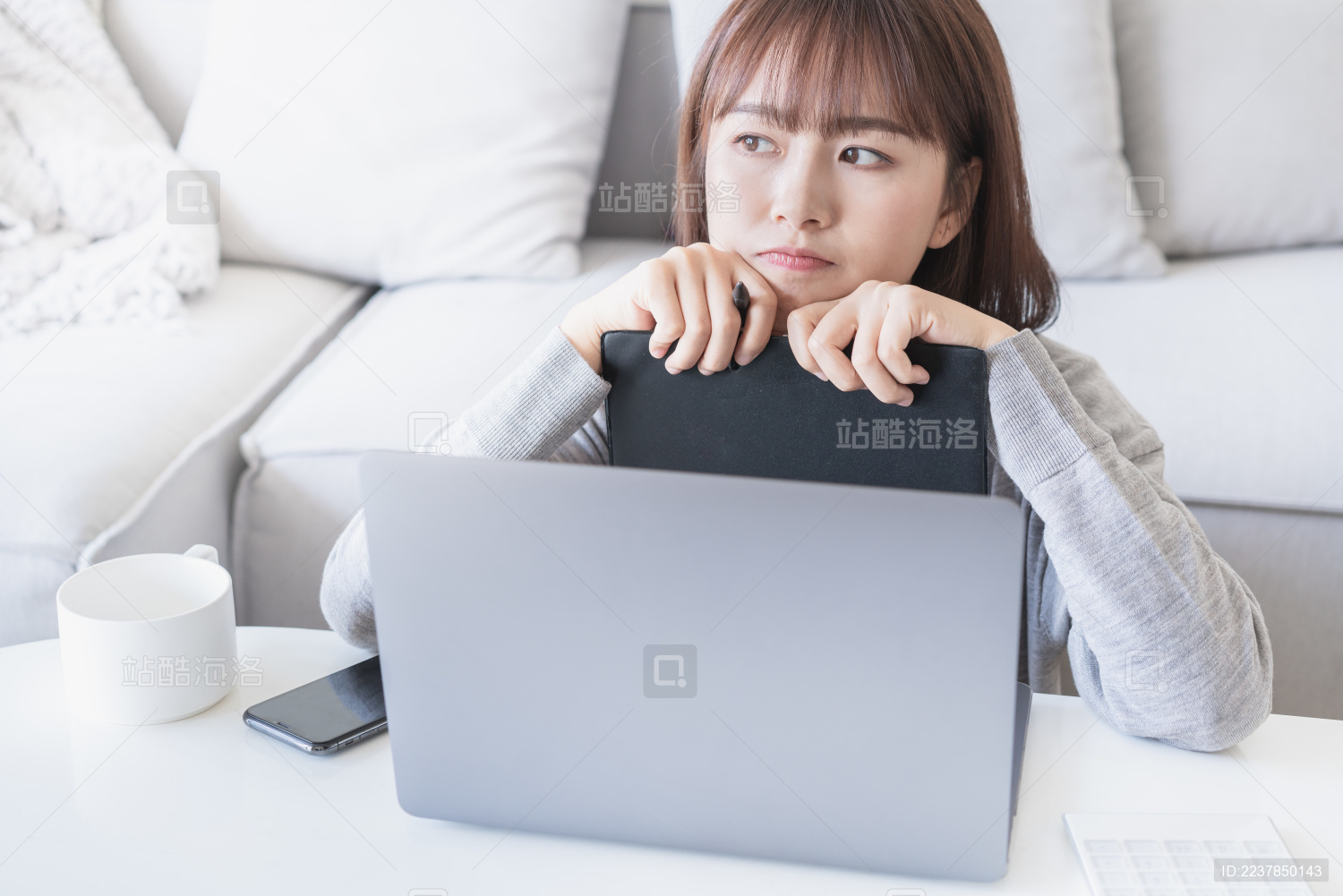 女生在电脑前将下巴抵在本子上思考