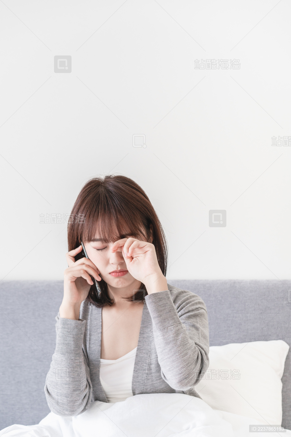 坐在床上一边接电话一边揉眼睛的亚洲女性