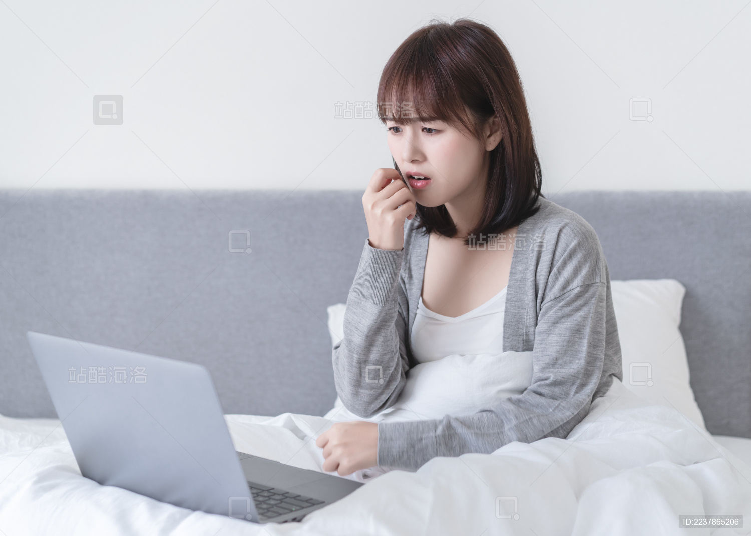 亚洲女性坐在床上一边看电脑一边害怕捂嘴
