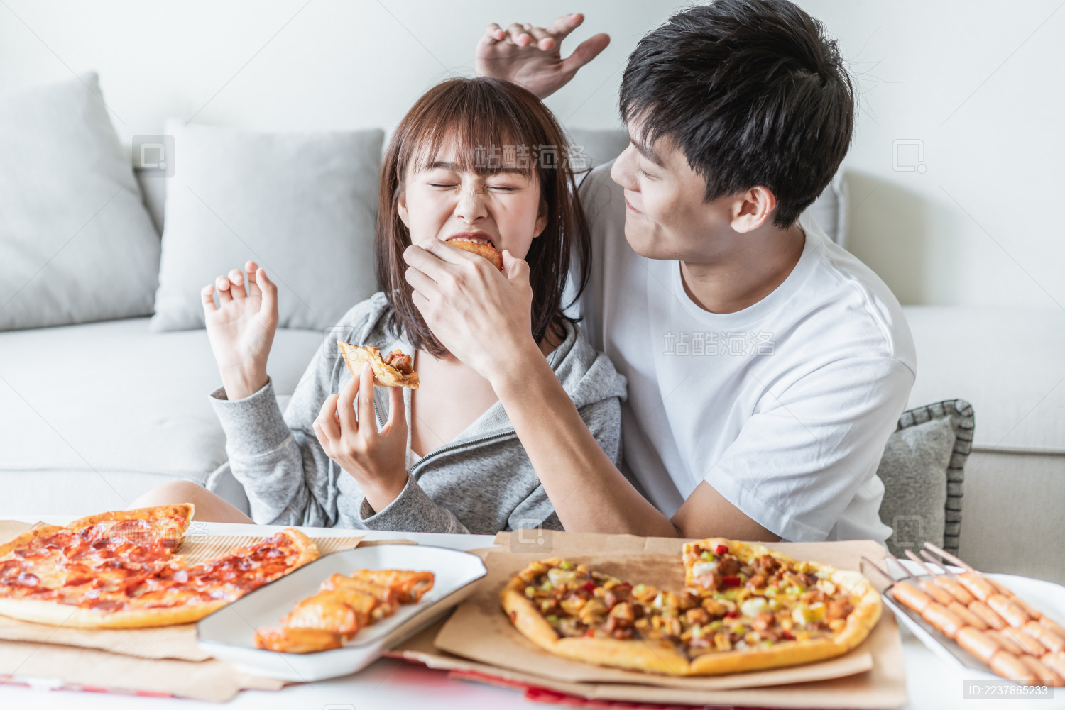年轻情侣在客厅一边打闹一边吃披萨