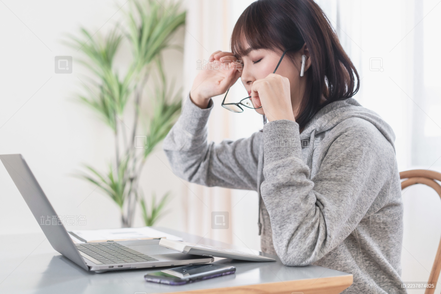 年轻女性在电脑旁摘下眼镜揉眼睛