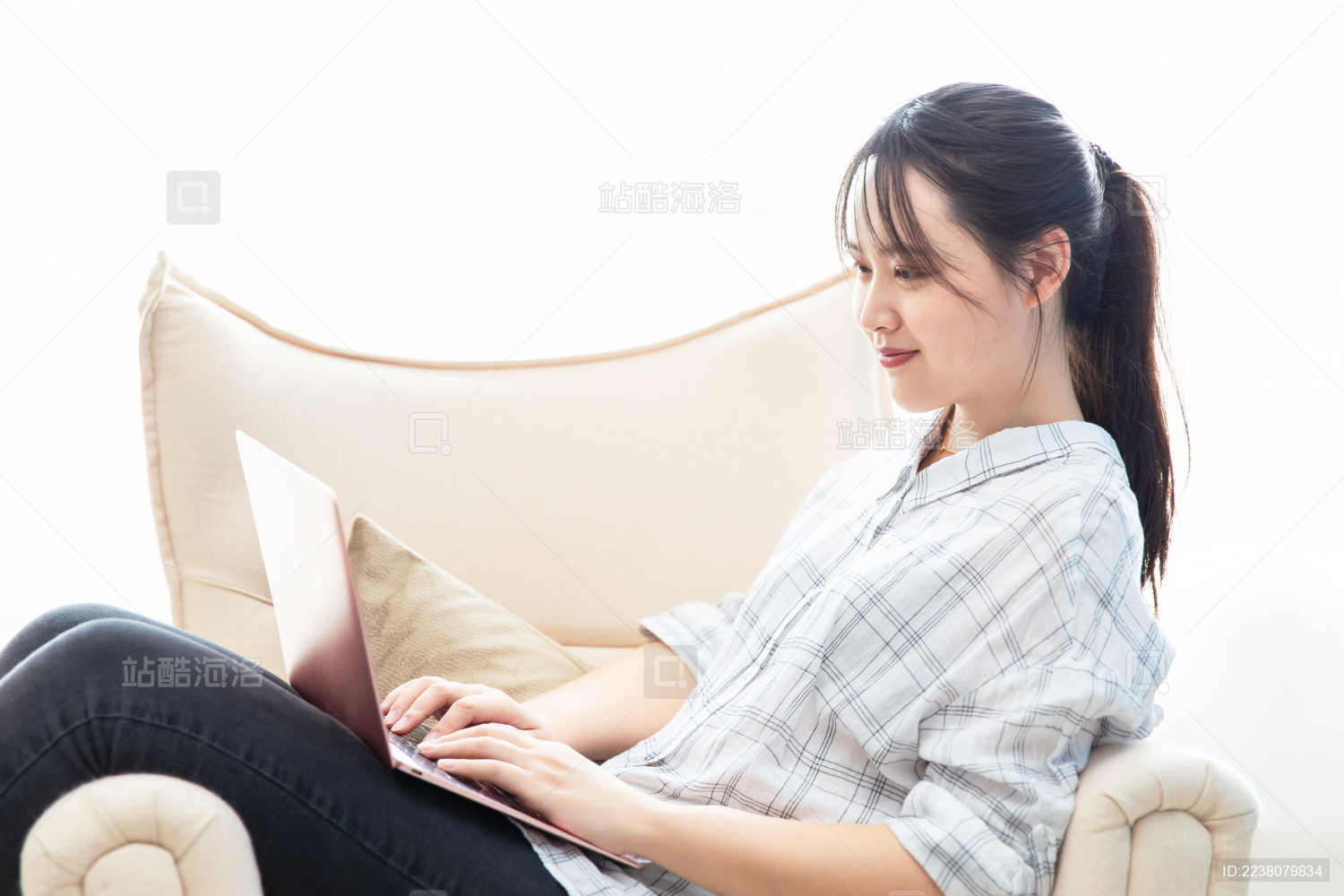 扎马尾的东方女生坐在沙发上使用笔记本电脑