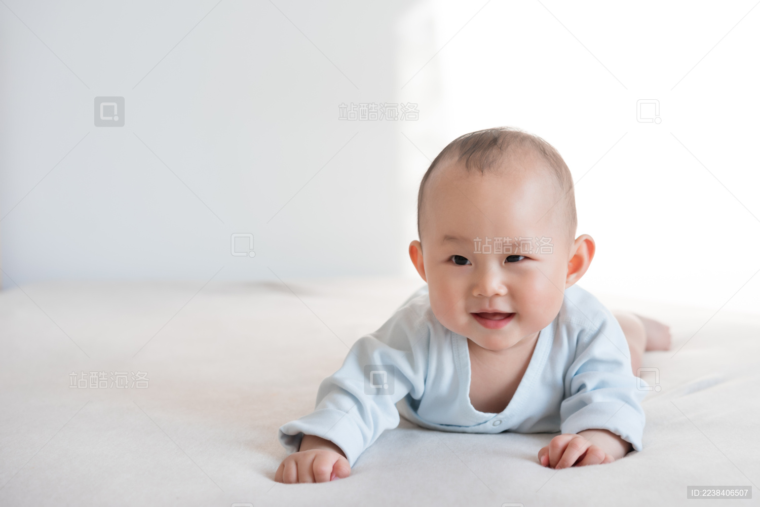 穿粉蓝和尚衣的九个月婴儿趴卧着笑