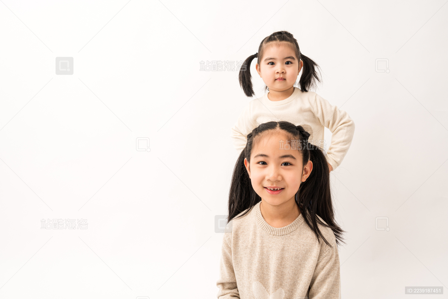 两名坐在白色背景前玩耍的姐妹